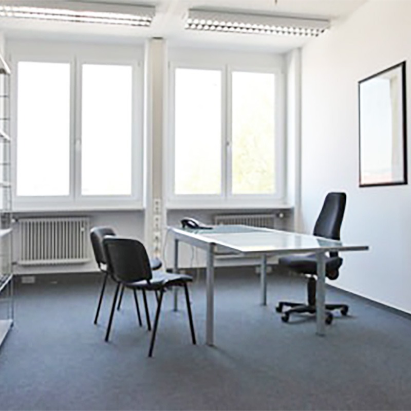 Ein möbliertes, modernes, helles Büro mit hohen Fenstern und dunkelblauem Teppichboden.